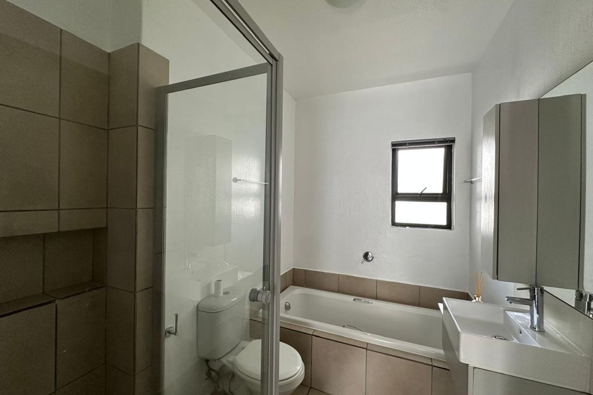 A clean, functional bathroom featuring a shower enclosure, bathtub, vanity basin, and neutral tiling throughout.