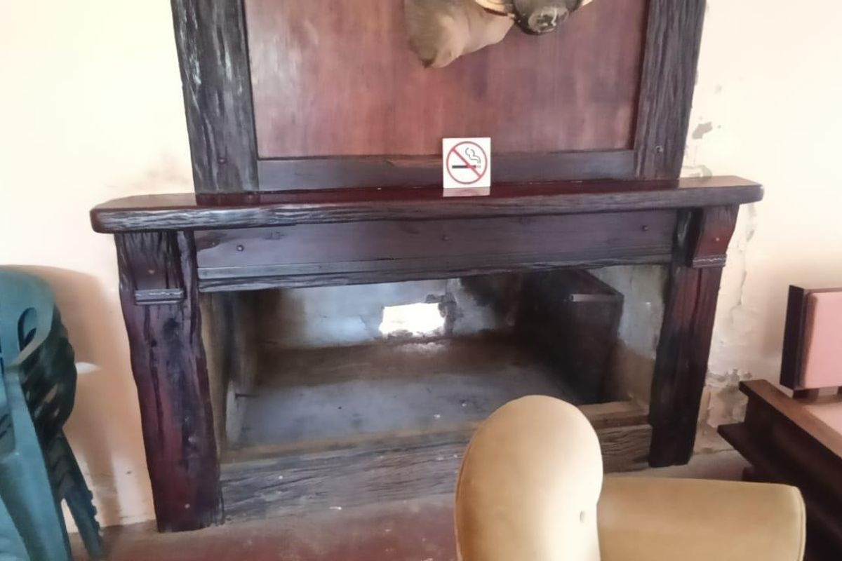 A rustic living room featuring a large, dark wood-framed fireplace with visible structural damage to the rear masonry.