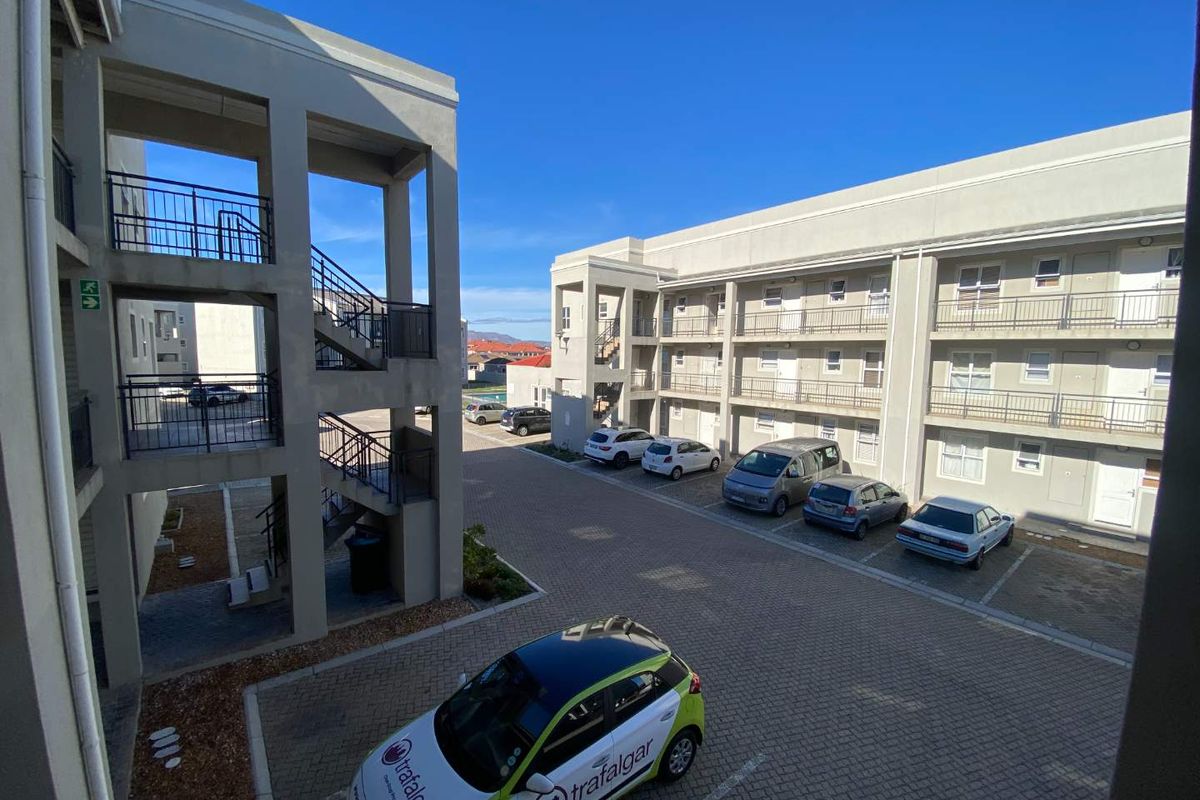Exterior view of a modern apartment complex featuring paved parking areas, multi-level stairwells, and balcony access for residential units.