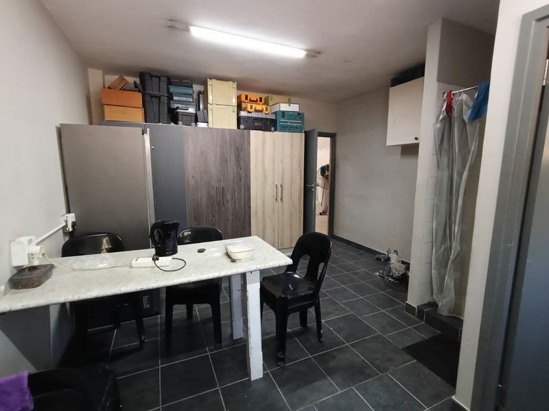 A functional utility space featuring tiled flooring, built-in storage cabinetry, and overhead fluorescent lighting, suitable for various industrial or storage purposes.