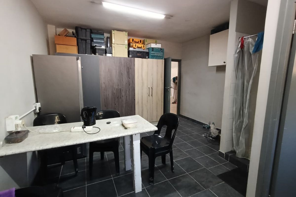 A functional utility space featuring tiled flooring, built-in storage cabinetry, and overhead fluorescent lighting, suitable for various industrial or storage purposes.