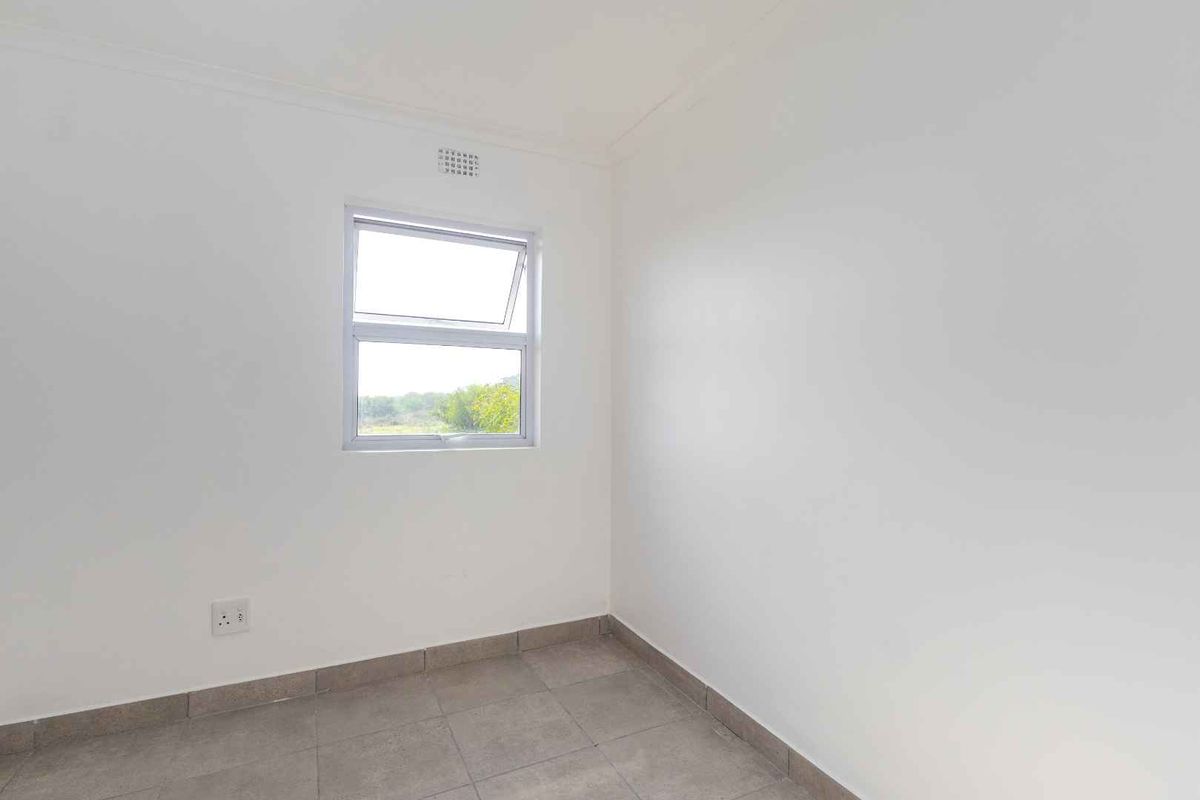 A clean, empty bedroom featuring neutral tiled flooring, white walls, and a single window providing natural light.