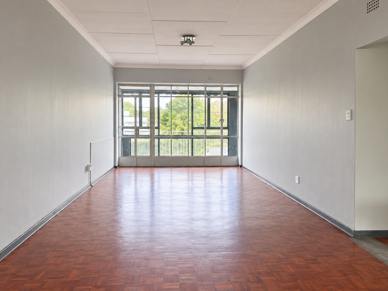A spacious, empty living area featuring classic parquet flooring, neutral walls, and large glass doors that provide ample natural light.
