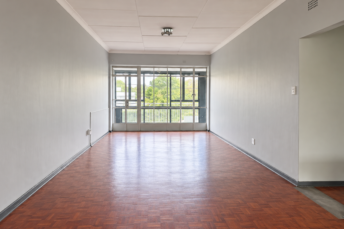 A spacious, empty living area featuring classic parquet flooring, neutral walls, and large glass doors that provide ample natural light.