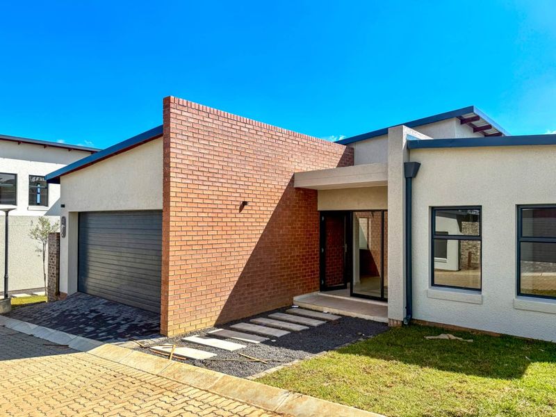 Modern cluster home featuring a striking brick facade, double garage, and a clean, contemporary entrance with paved walkway.