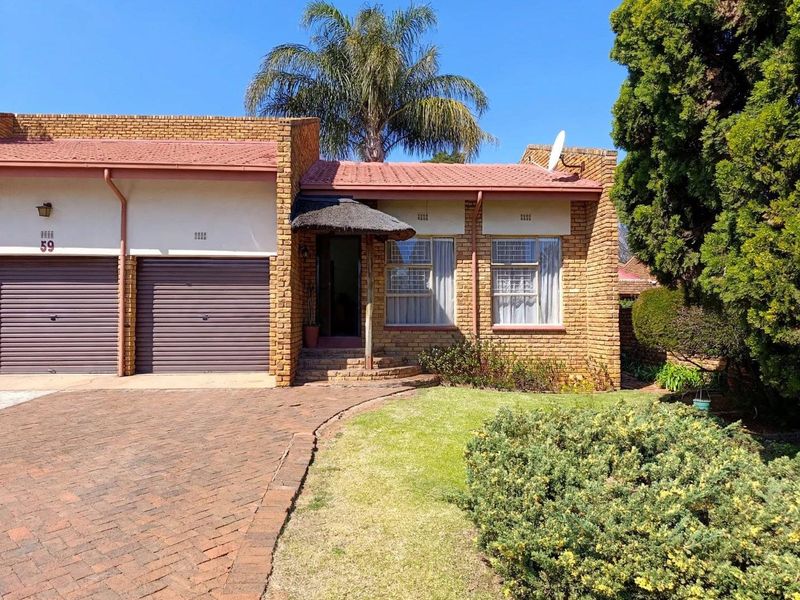 Front elevation of a face brick cottage featuring a double garage with roller doors, a paved driveway, and a small thatched entrance canopy.