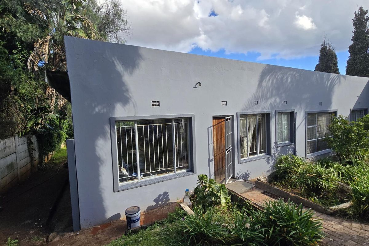 Rear exterior view of the house featuring a painted facade, security bars on windows, and a paved walkway leading to the entrance.