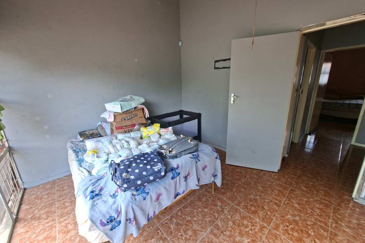 A bedroom featuring tiled flooring and neutral wall finishes, providing a functional space with direct access to the hallway.