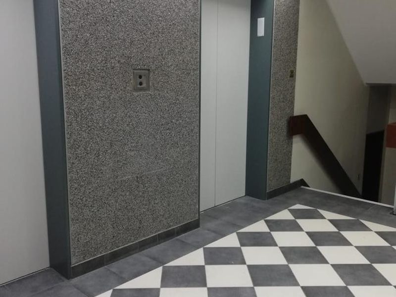 A clean office building elevator lobby featuring checkered tile flooring, modern elevator doors, and access to a stairwell.