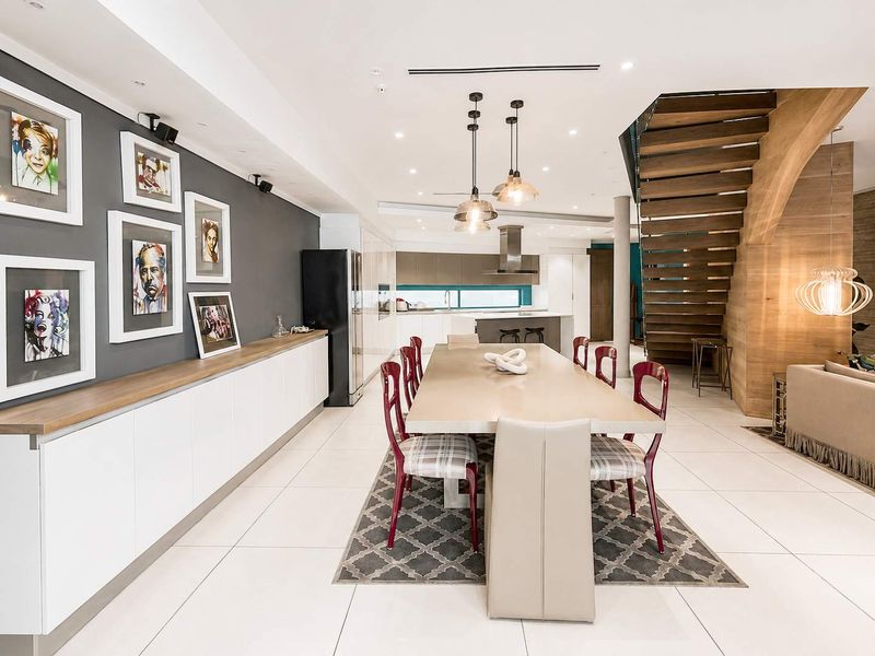 Spacious open-plan living and dining area featuring modern tiled floors, custom built-in cabinetry, and a striking timber staircase leading to the upper level.