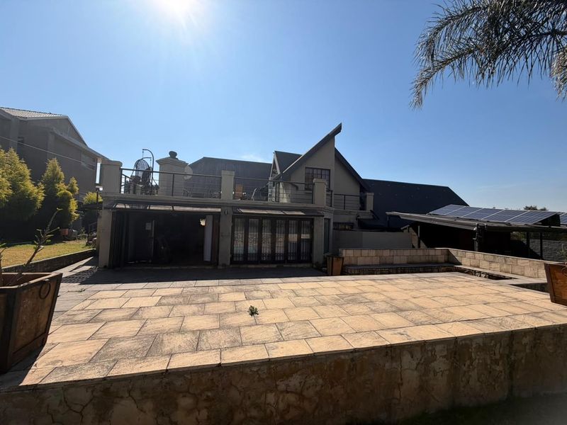 Rear view of the property featuring a paved patio area, elevated balcony with metal railings, and solar panels installed on the roof.