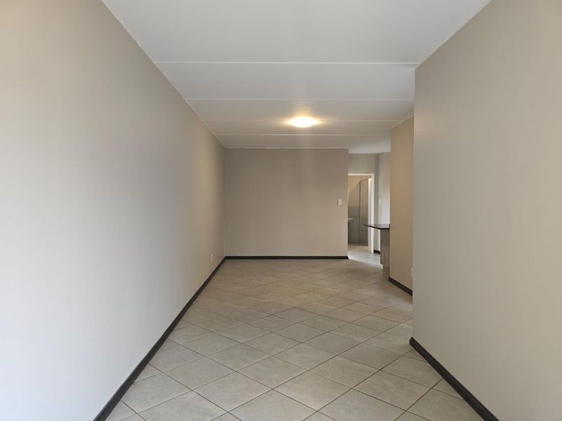 An empty, open-plan living area featuring neutral wall tones, tiled flooring, and clean finishes, providing a versatile space for various interior design layouts.