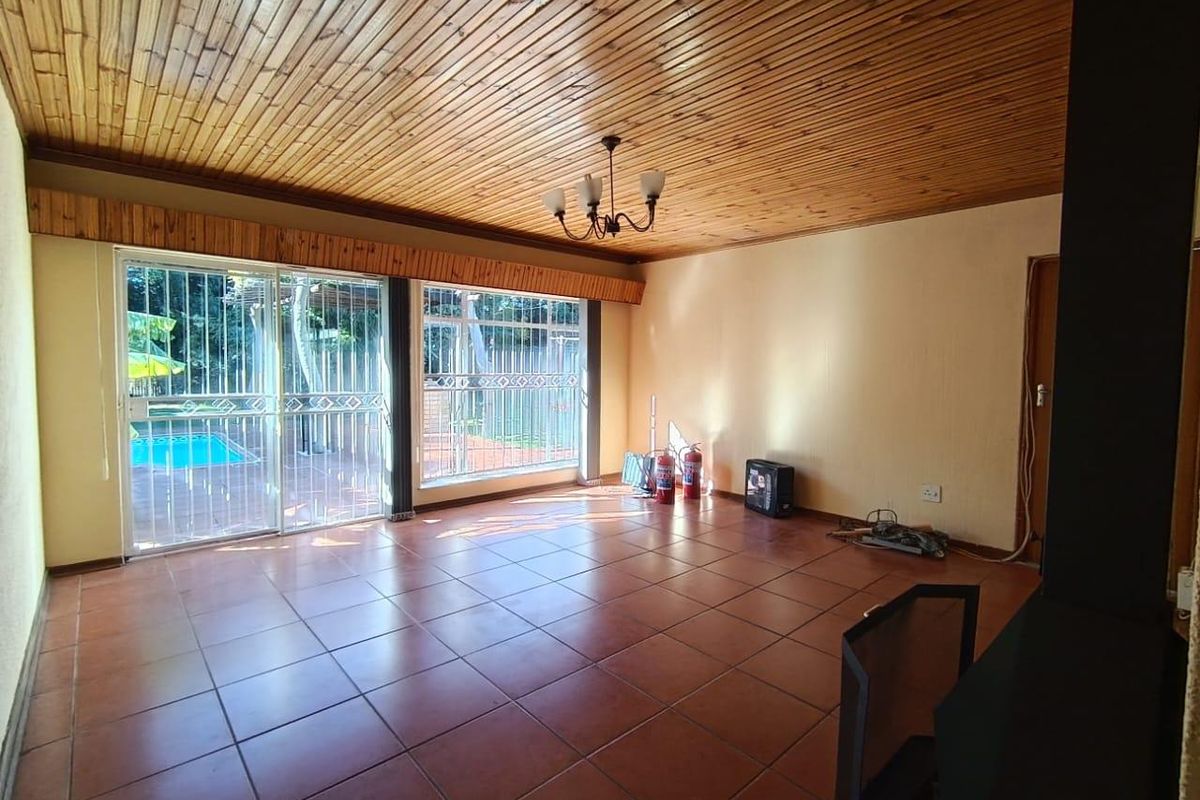 Spacious living area featuring terracotta floor tiles, a timber-clad ceiling, and large sliding glass doors providing direct access to the outdoor pool area.