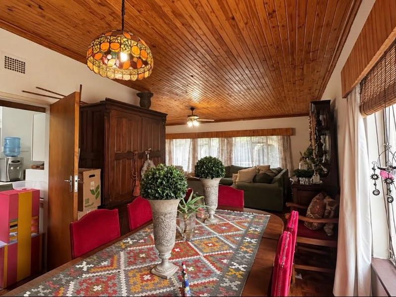 Dining room featuring a warm timber tongue and groove ceiling, ceiling fan, and large windows with security bars, offering a view into the adjacent kitchen.