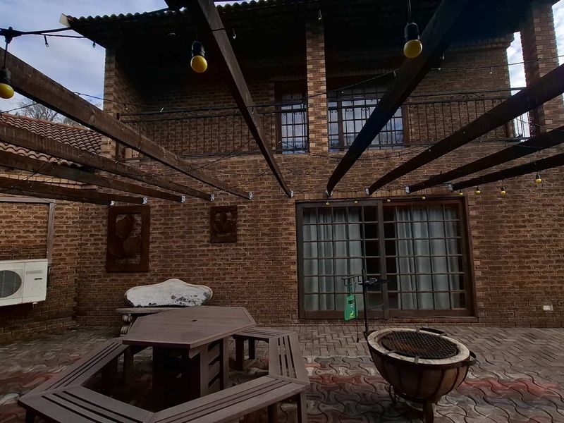 A spacious outdoor patio area featuring a timber pergola, paved flooring, and direct access to the main house through sliding glass doors.