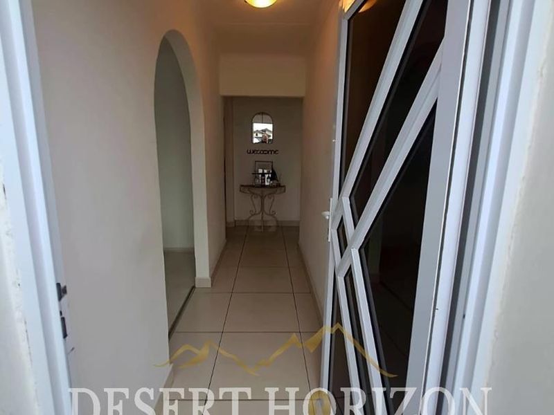 A clean, tiled hallway featuring an arched entryway and a secure metal gate, providing a bright and functional transition space within the home.