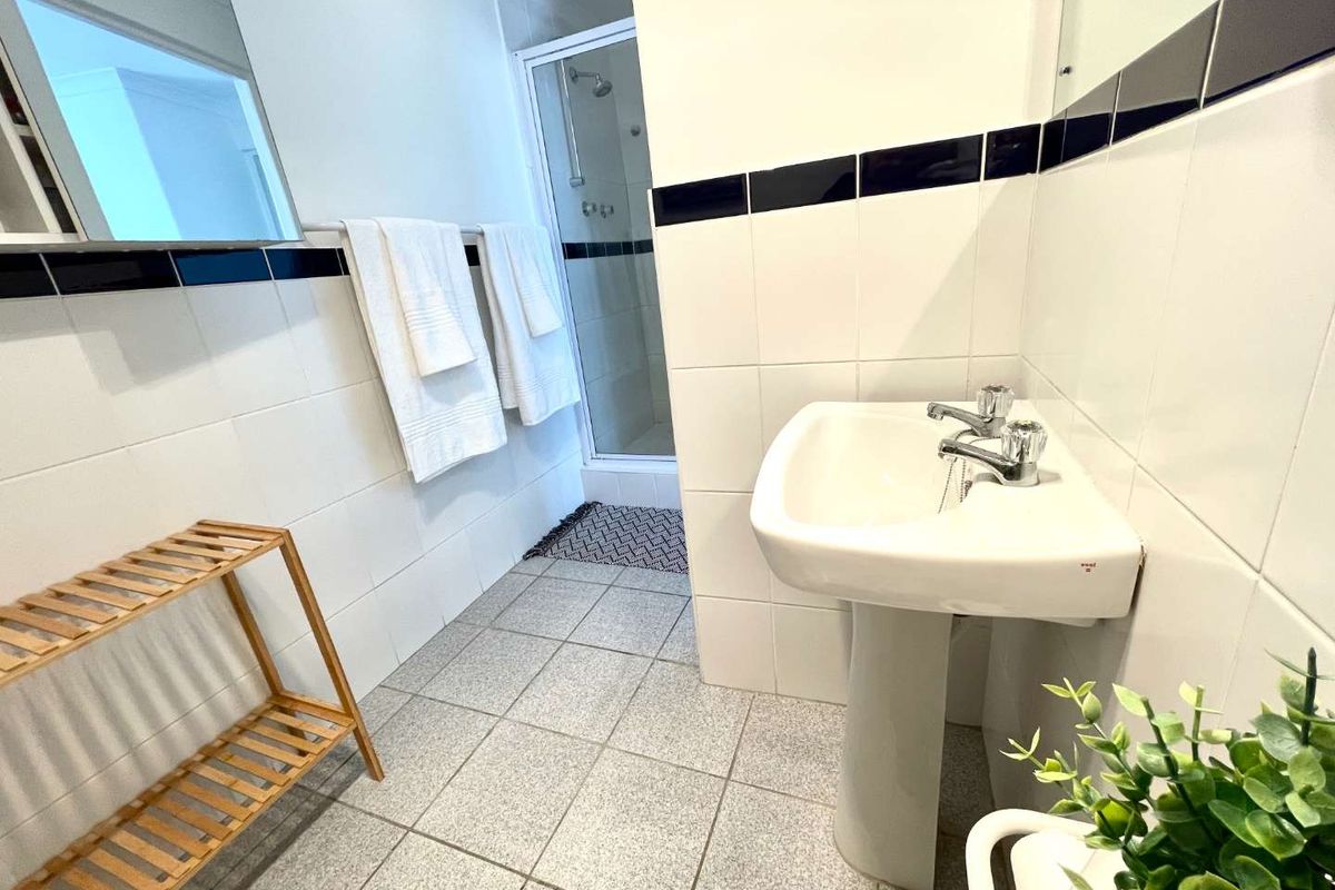 A functional bathroom featuring a pedestal basin, tiled walls with a decorative border, and a separate shower enclosure.