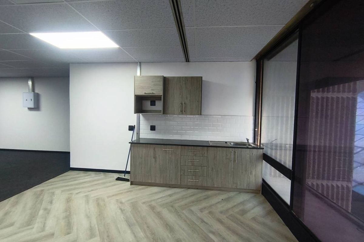 A modern office kitchenette featuring wood-grain cabinetry, a dark countertop, stainless steel sink, and white subway tile backsplash.