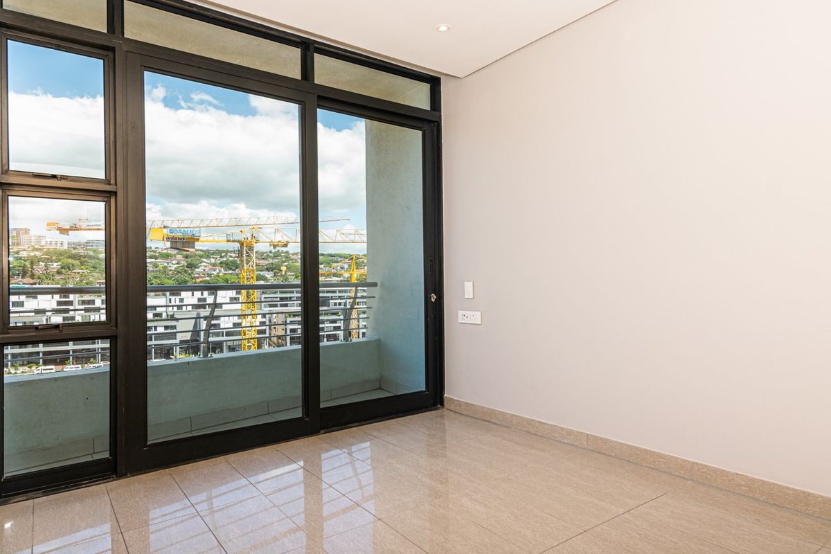 A bright, empty living area featuring large sliding glass doors that open onto a private balcony with urban views.