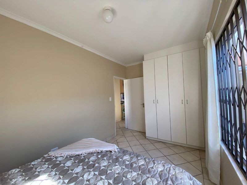 A bedroom featuring tiled flooring, built-in cupboards, and a window fitted with a security gate.