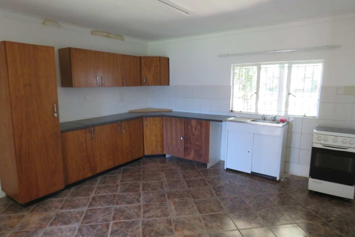A functional kitchen featuring wood-finish cabinetry, tiled flooring, a stainless steel sink, and a freestanding stove, offering a blank canvas for renovation.
