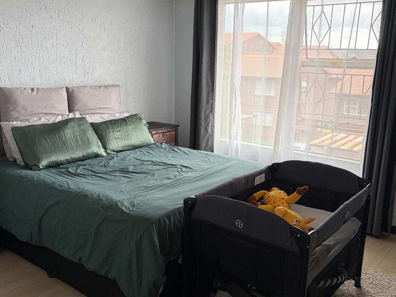 A bedroom featuring laminate flooring and a window fitted with security bars, offering a functional space with natural light.