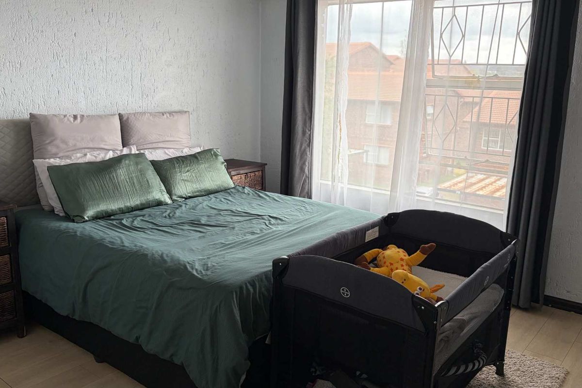 A bedroom featuring laminate flooring and a window fitted with security bars, offering a functional space with natural light.