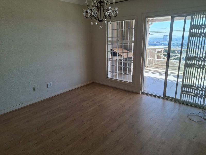 An empty living room featuring laminate flooring, a chandelier, and a sliding glass door providing access to a balcony with exterior views.