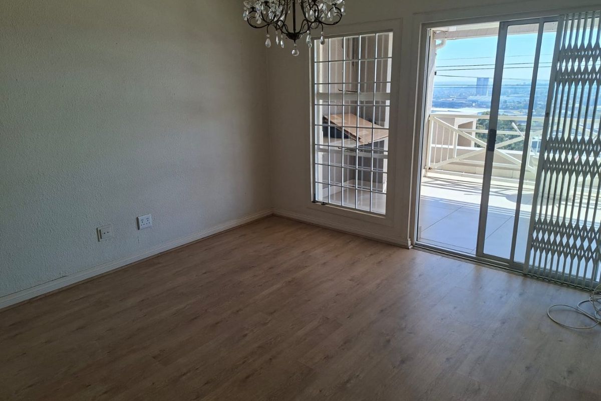 An empty living room featuring laminate flooring, a chandelier, and a sliding glass door providing access to a balcony with exterior views.