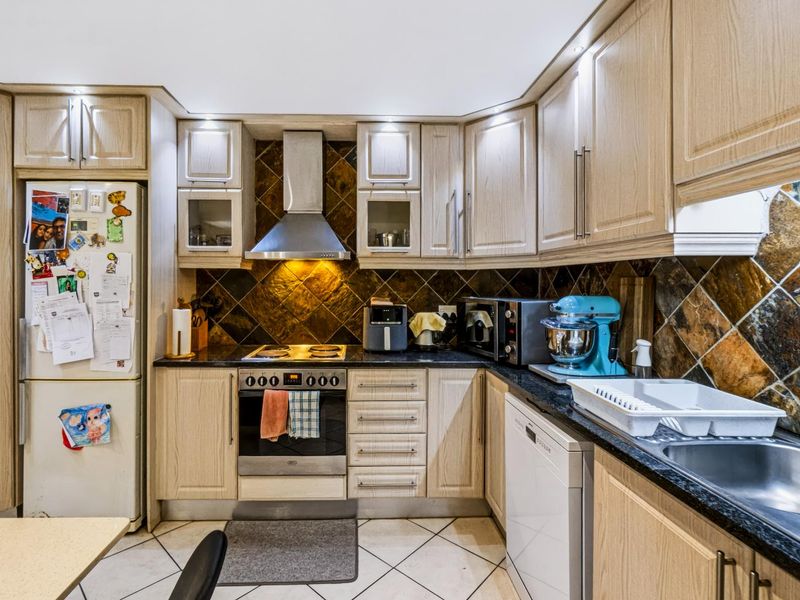 A functional kitchen featuring light wood cabinetry, granite countertops, a stone tile backsplash, and integrated appliances including an oven and extractor fan.