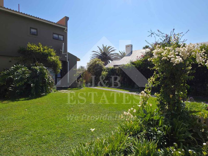 A well-maintained rear garden featuring a lush lawn, established landscaping, and a view of the property's rear elevation.