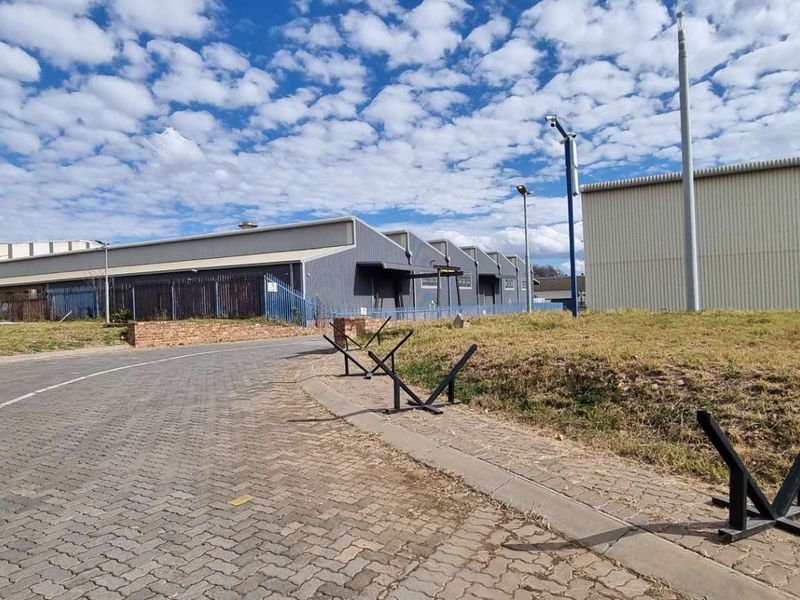 Exterior view of an industrial facility featuring metal cladding, paved access road, and security perimeter fencing.