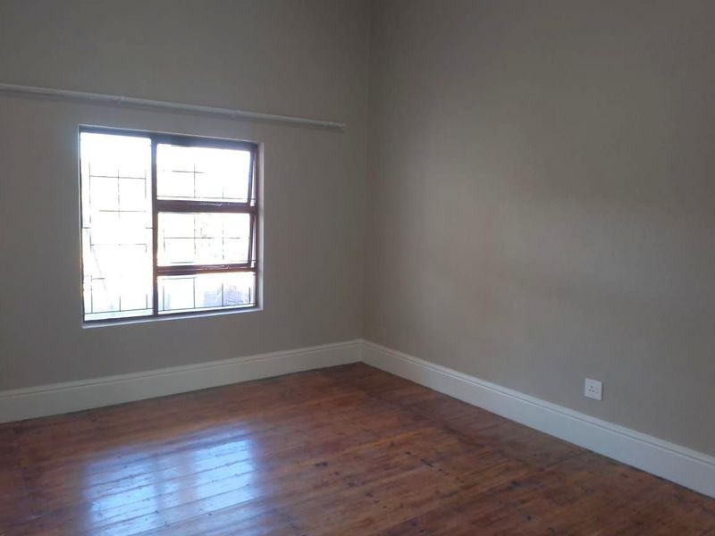 An empty bedroom featuring polished timber flooring, neutral wall tones, and a window fitted with security bars.
