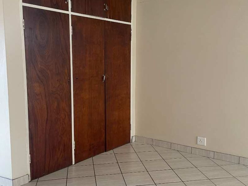 An empty bedroom featuring tiled flooring and built-in wooden cupboards, offering a blank canvas for potential interior updates.