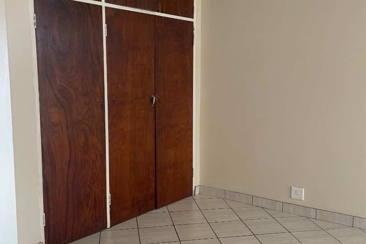 An empty bedroom featuring tiled flooring and built-in wooden cupboards, offering a blank canvas for potential interior updates.