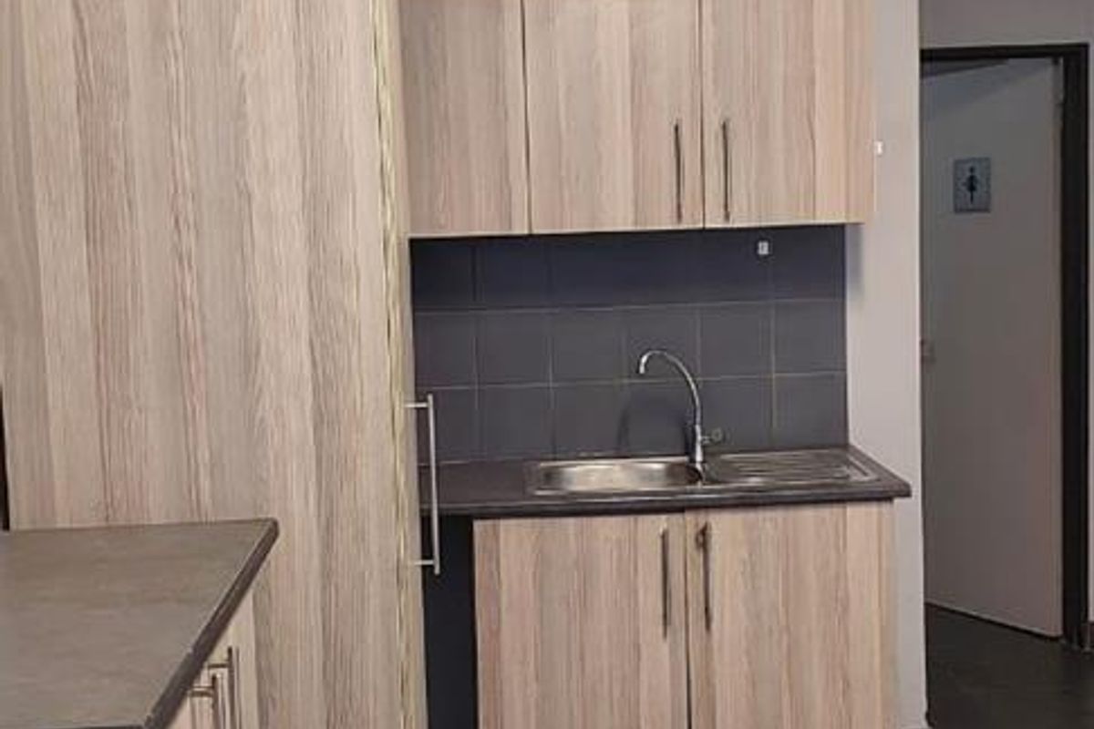 Compact kitchenette featuring light wood-grain cabinetry, dark laminate countertops, a stainless steel sink, and dark tiled flooring.