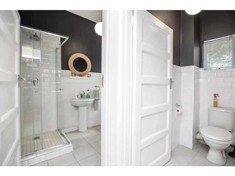 A clean, modern bathroom featuring a glass shower enclosure, pedestal basin, and toilet with classic white subway tiling and contrasting dark walls.