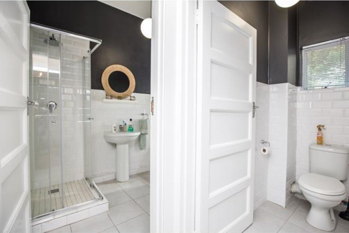 A clean, modern bathroom featuring a glass shower enclosure, pedestal basin, and toilet with classic white subway tiling and contrasting dark walls.