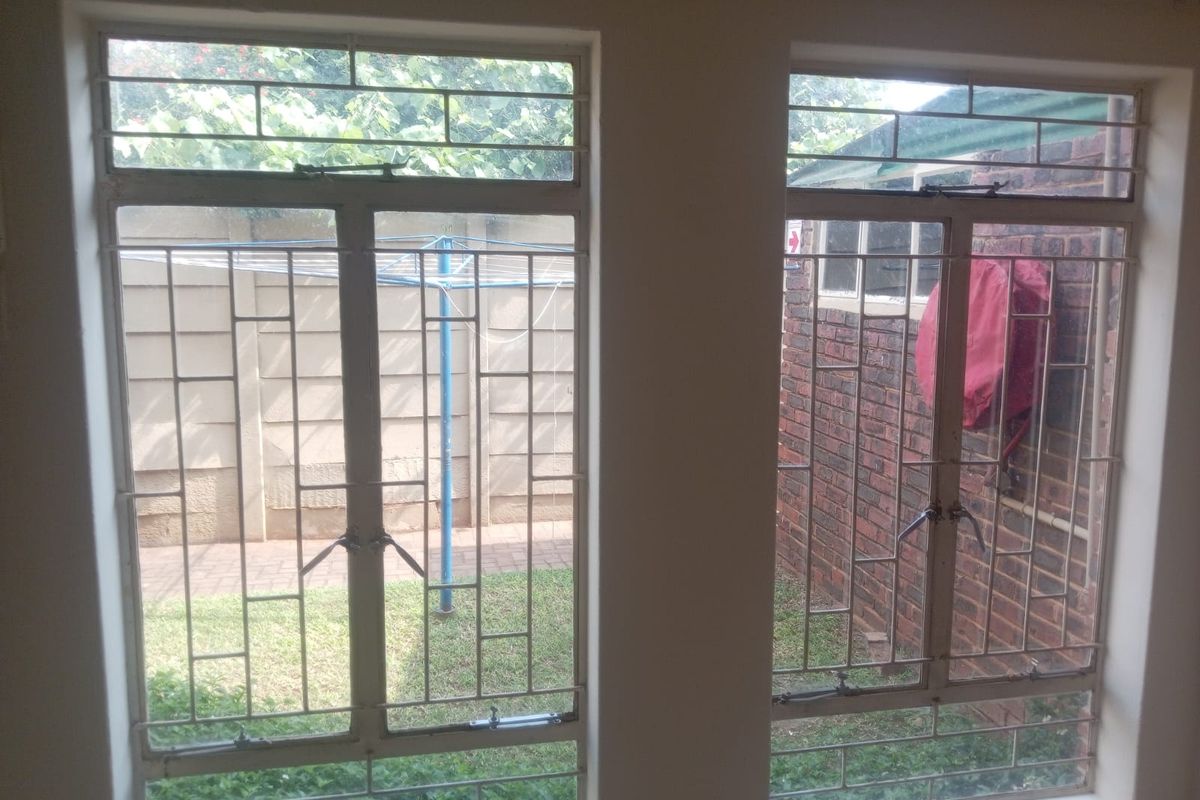Interior view of a bedroom featuring steel-framed windows with security bars, overlooking a rear garden area.
