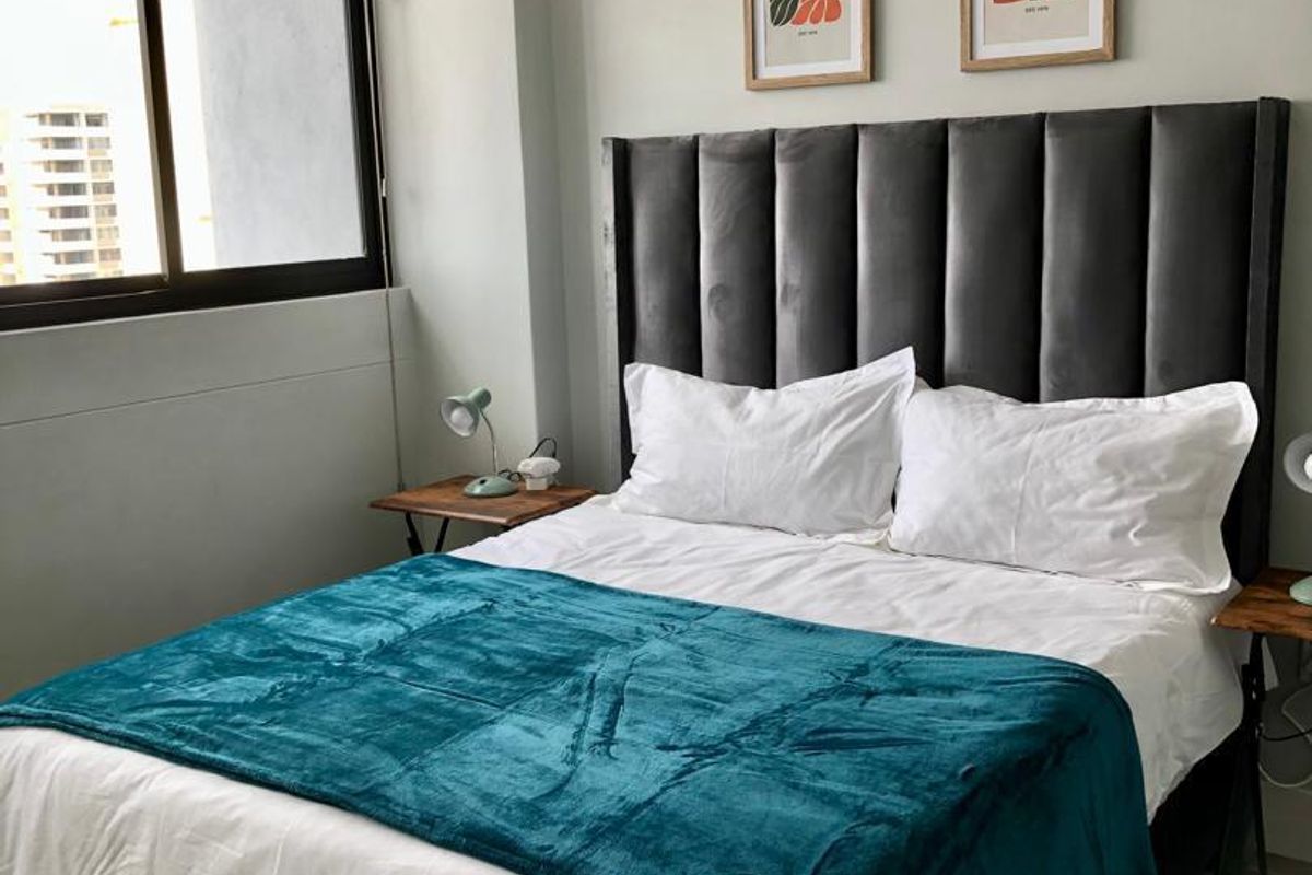 A well-maintained bedroom featuring neutral walls, modern laminate flooring, and a large window with fitted blinds providing natural light.