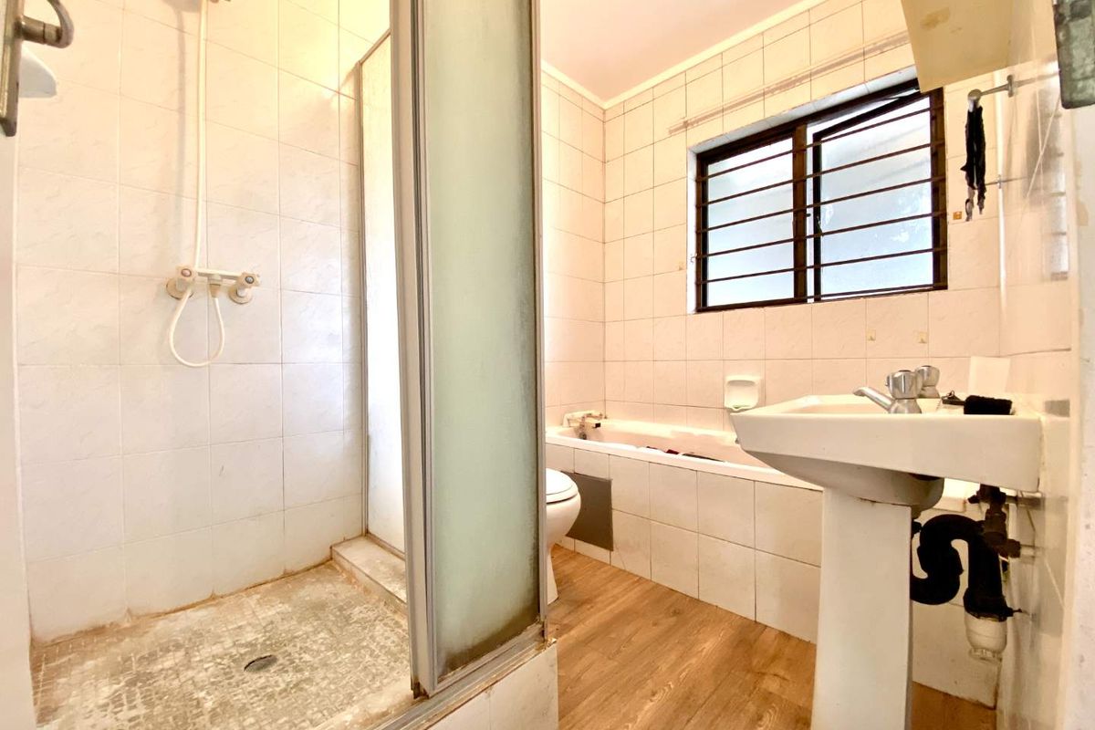 A dated bathroom featuring a separate shower and bathtub, pedestal sink, and tiled walls, requiring cosmetic updates to modernize the space.