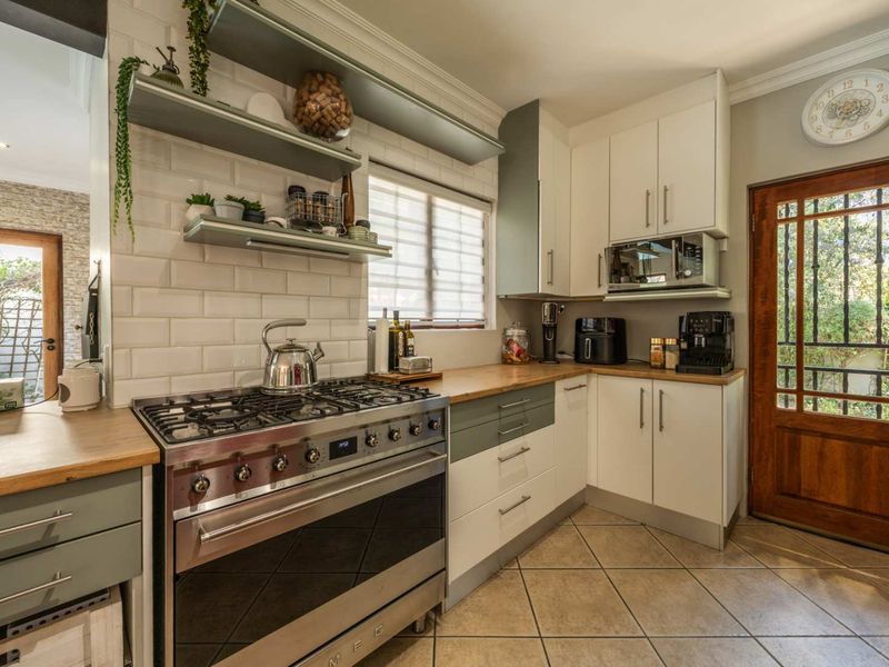 A well-appointed kitchen featuring a gas stove, subway tile backsplash, wooden countertops, and ample built-in cabinetry with a classic timber door.