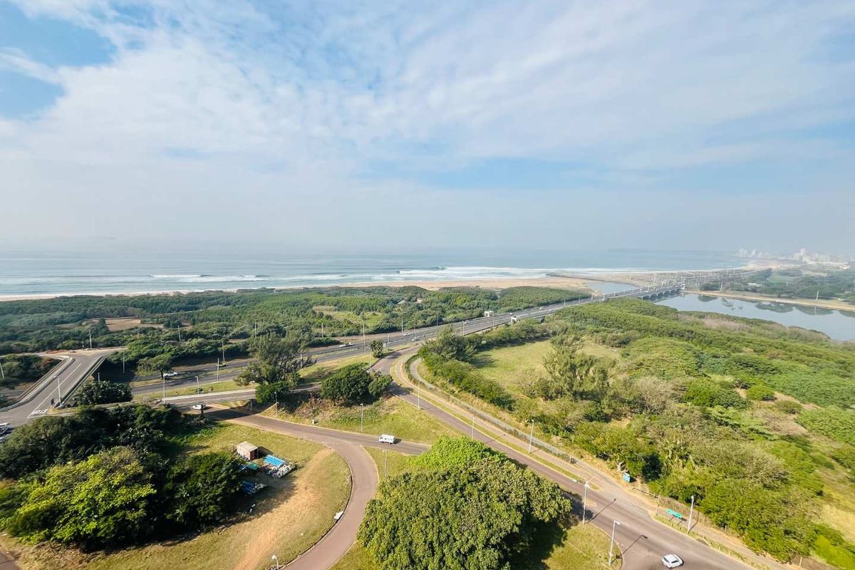 Elevated aerial view showcasing the surrounding coastal landscape, including the ocean, beach, natural vegetation, and local road infrastructure.