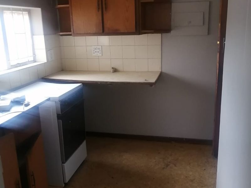A compact, dated kitchen featuring wooden cabinetry, a tiled backsplash, and a freestanding stove, offering potential for modernization and renovation.