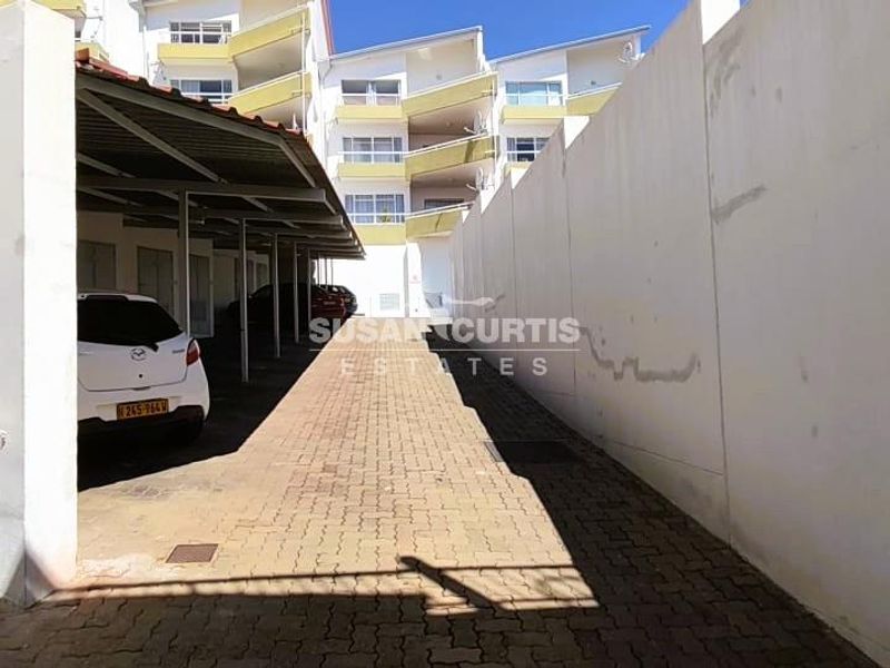 A covered parking area within an apartment complex featuring paved ground and high boundary walls.