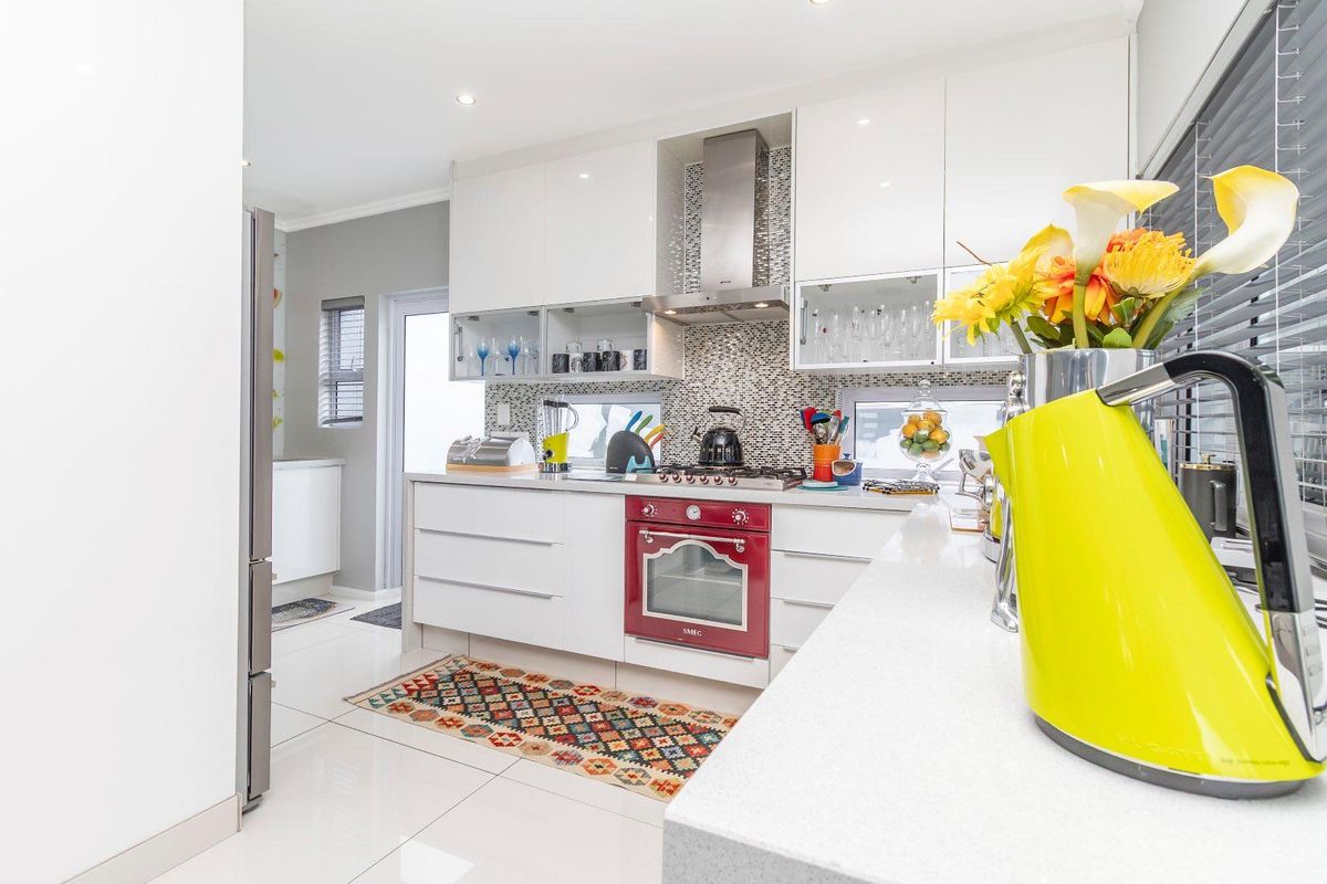 Modern kitchen featuring high-gloss white cabinetry, stone countertops, a mosaic tile backsplash, and a built-in stainless steel extractor fan with a red oven.