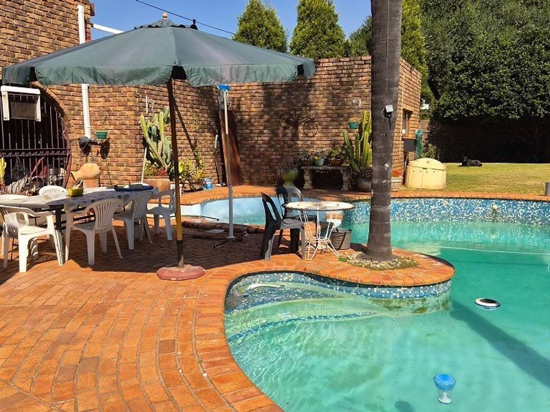Outdoor pool area featuring a curved swimming pool with mosaic tiling, surrounded by brick paving and a rustic brick boundary wall.