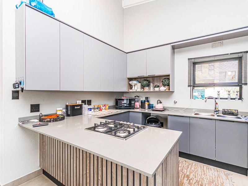 Modern kitchen featuring grey cabinetry, stone countertops, a built-in gas hob, and a stainless steel sink with a window view.