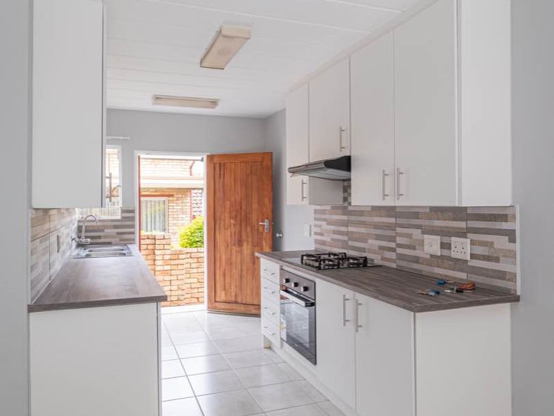 A clean, functional kitchen featuring white cabinetry, wood-look laminate countertops, a gas hob, and direct access to the exterior.