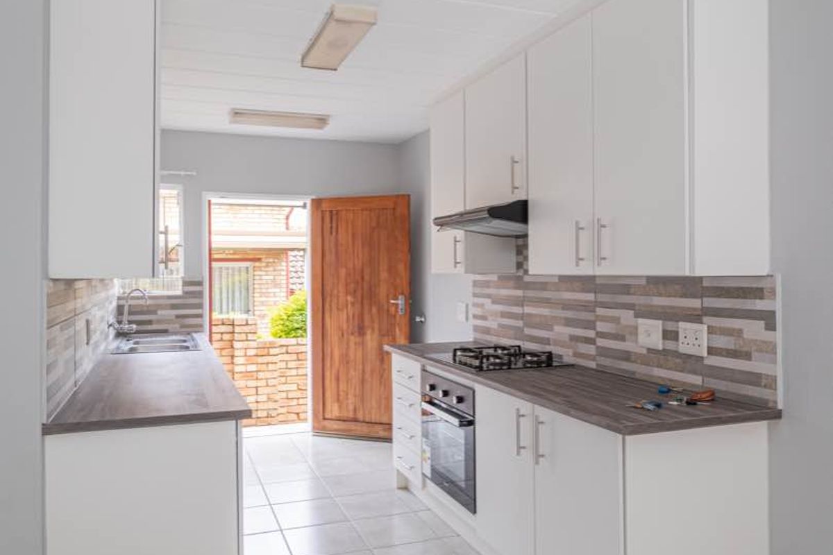 A clean, functional kitchen featuring white cabinetry, wood-look laminate countertops, a gas hob, and direct access to the exterior.